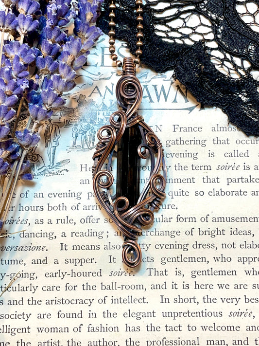 Decorative copper pendant with a black tourmaline crystal on on the page of an old book surrounded with lavender and lace.