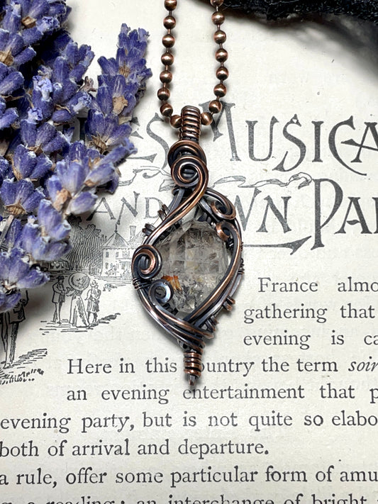 Copper necklace with a smokey quartz crystal pendant on an old book page with lavender flowers.